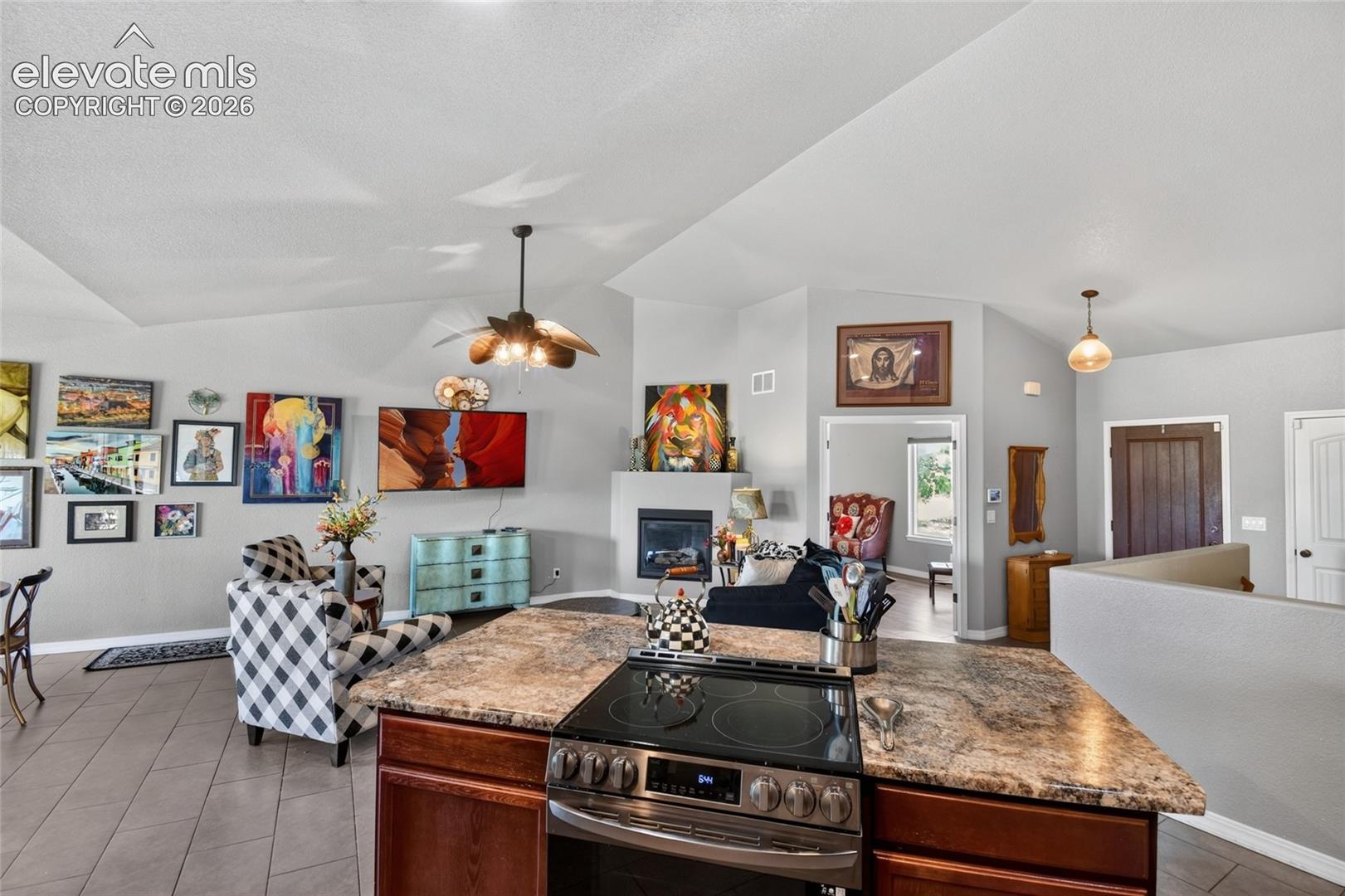 Kitchen island featuring a stone-look countertop, integrated electric cooktop, and dark wood-finish cabinetry, complemented by vaulted ceilings and a built-in fireplace