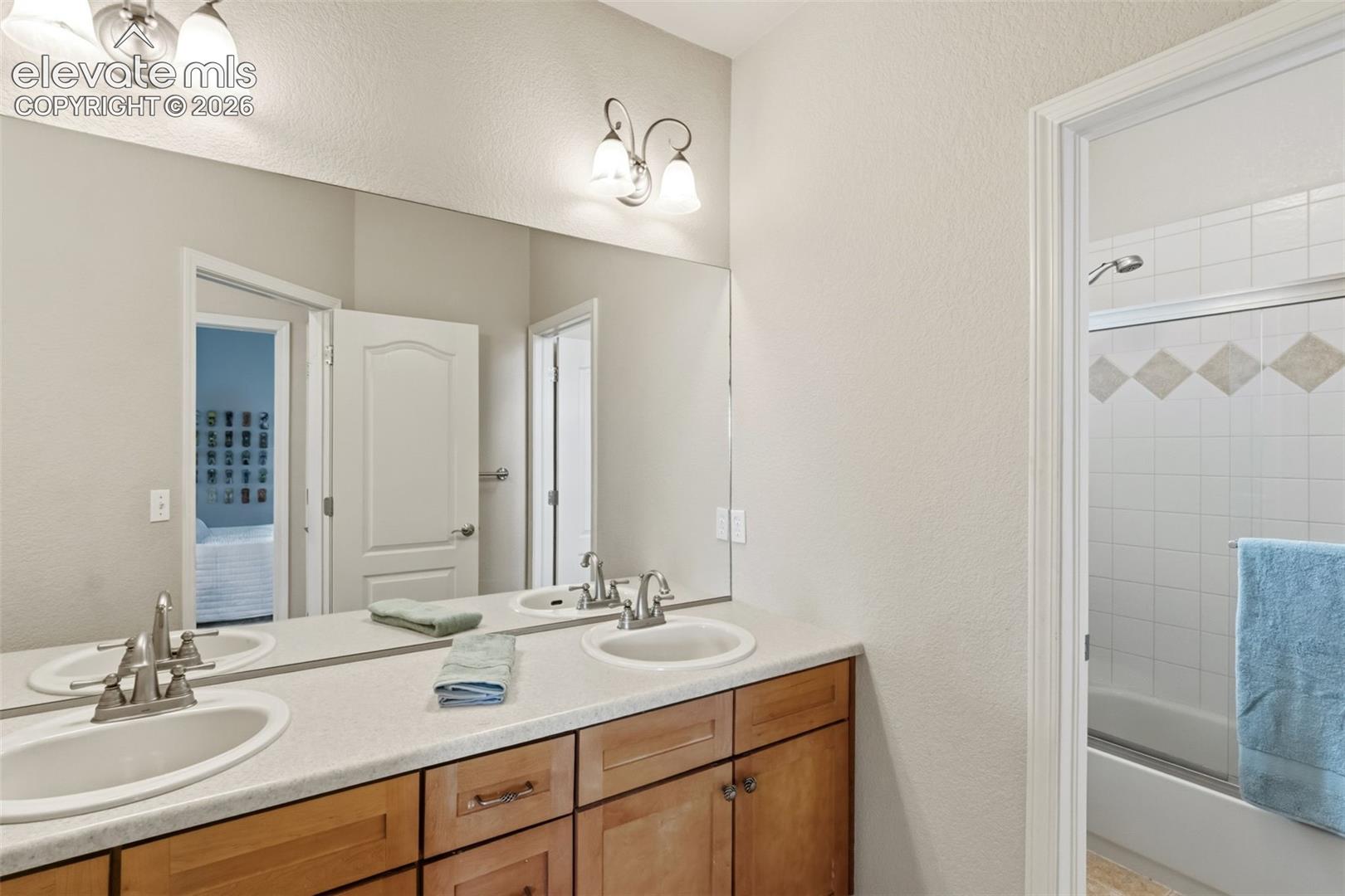 Bathroom featuring a dual vanity with wood-finish cabinetry, a large wall-mounted mirror, and a shower-over-tub combination with tiled surround