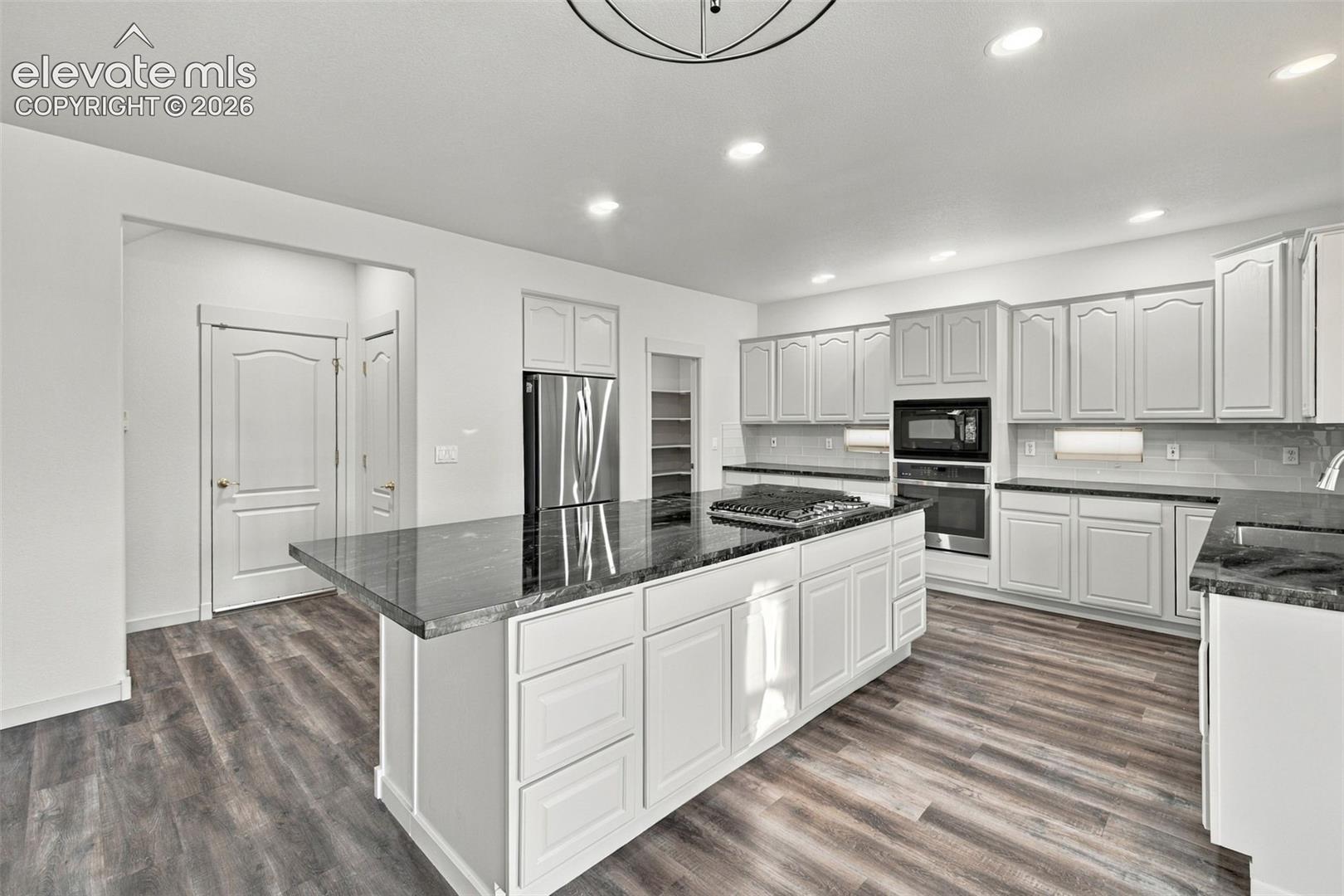 Kitchen featuring white shaker-style cabinetry, dark stone countertops, a center island with a built-in gas cooktop, stainless steel wall-mounted oven, and wood-finish flooring