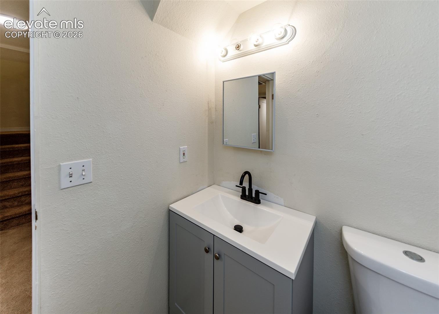 Vanity featuring a solid-surface countertop with an integrated sink, matte black faucet, cabinet storage, medicine cabinet, and wall-mounted light fixture