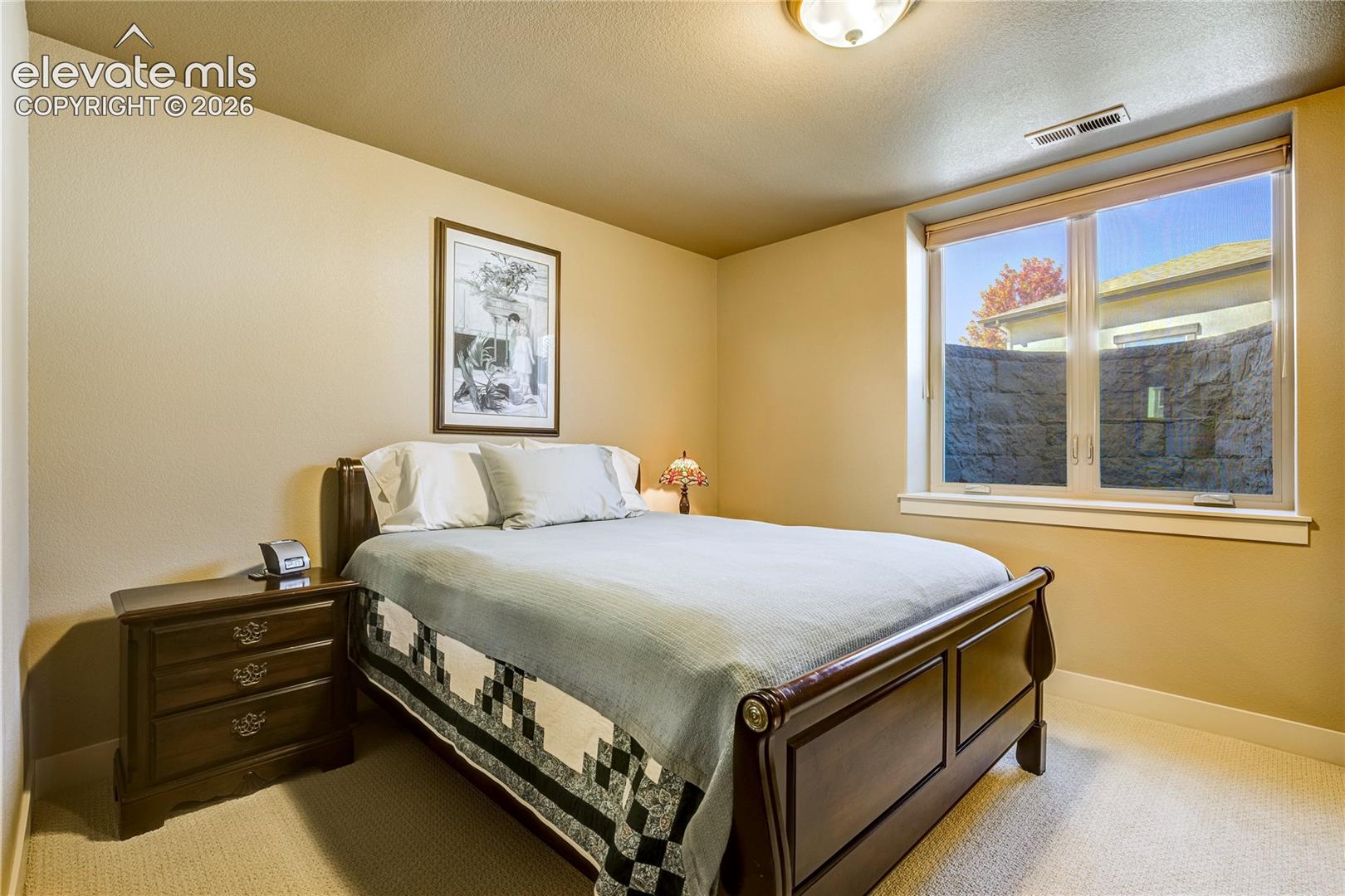 A spacious garden-level bedroom offers a comfortable retreat for guests or household members, with soft neutral finishes, generous natural light + convenient access to the lower-level living areas.