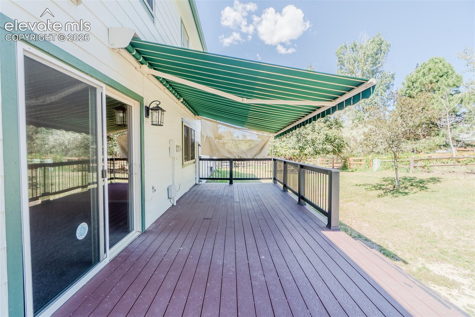Expansive outdoor deck with wood-finish flooring, black railings, and a green and white striped retractable awning