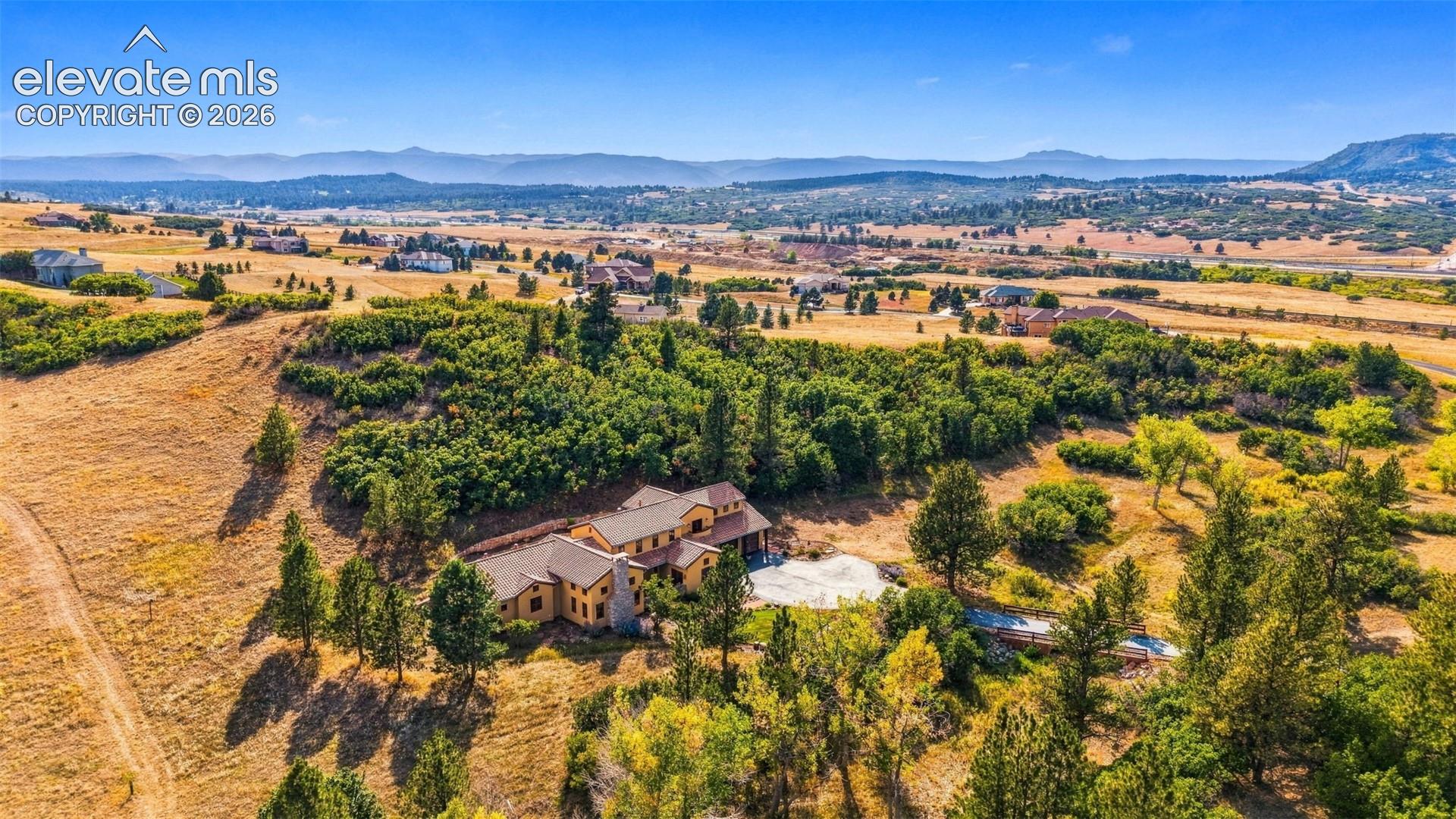 Expansive property featuring a multi-level residence, surrounding mature trees, and mountainous terrain