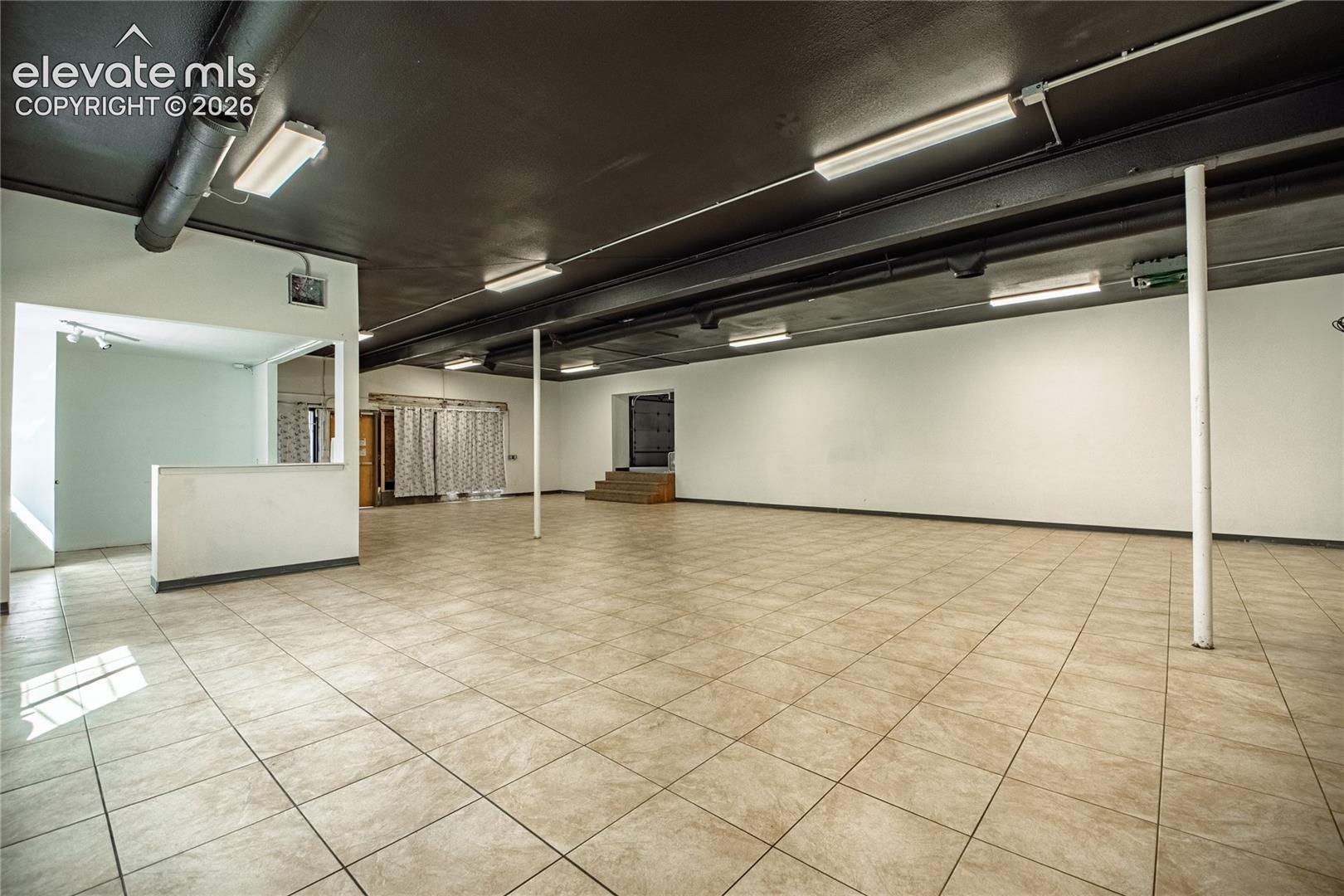Expansive open space featuring ceramic tile flooring, a painted black ceiling, and fluorescent lighting