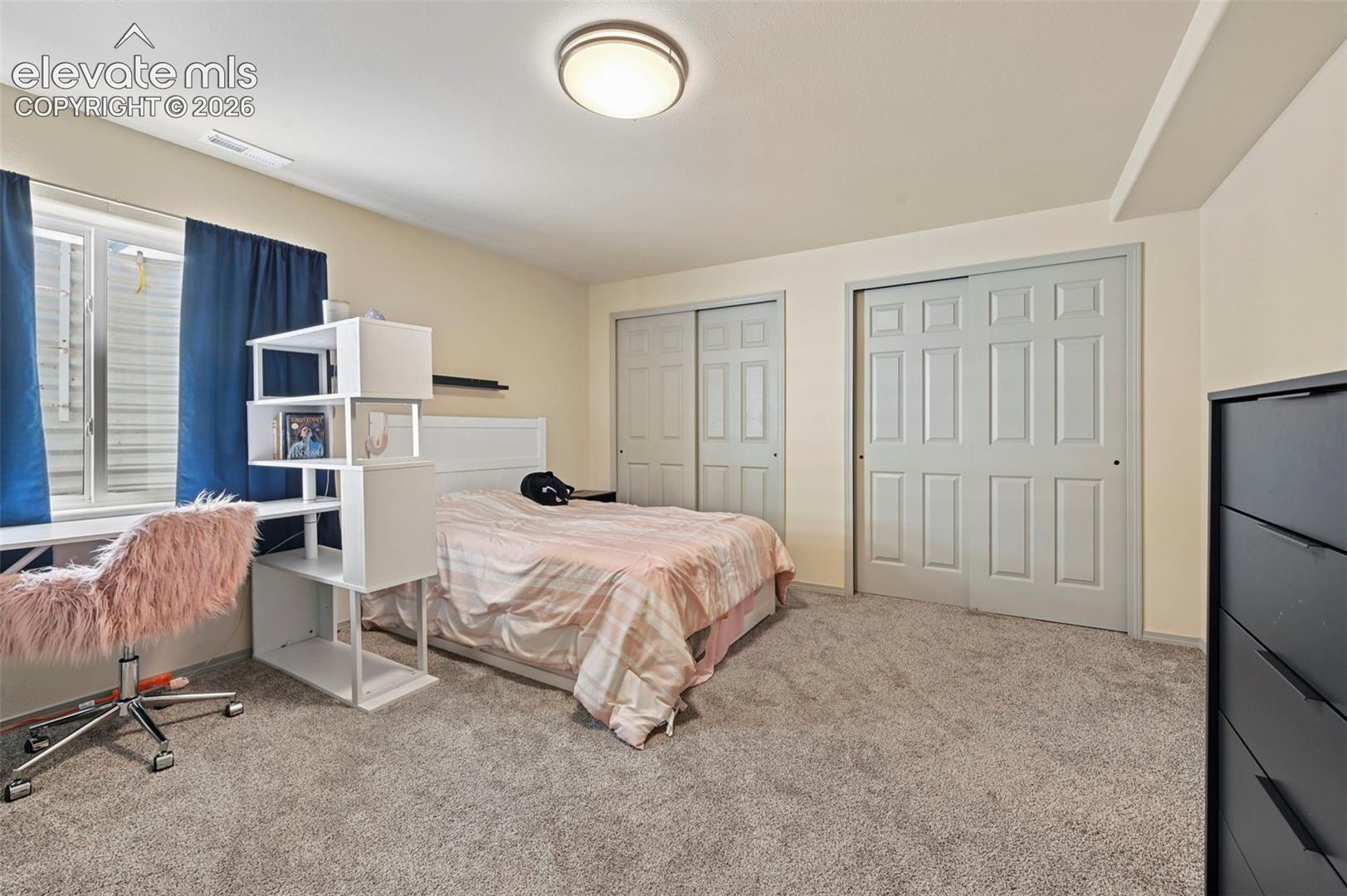 Spacious carpeted room featuring two panel sliding closet doors, a window with a sill, and a flush mount ceiling light