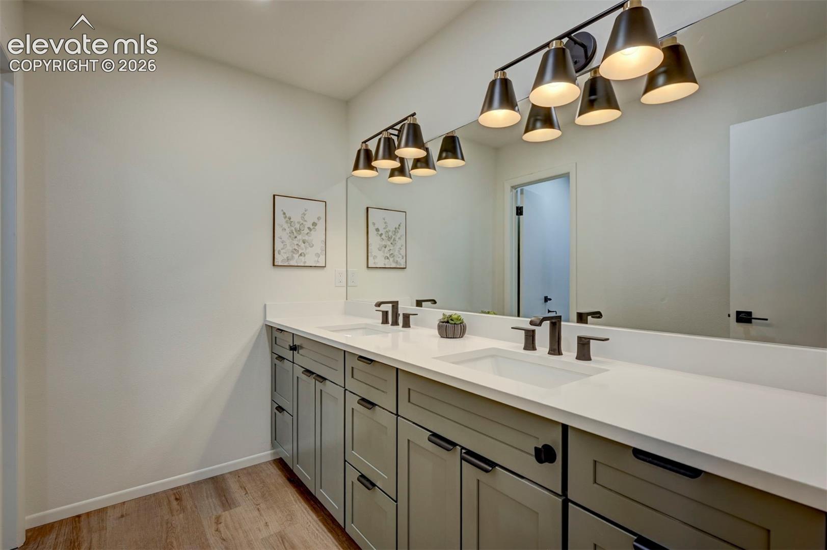 Dual-sink vanity featuring soft-toned cabinetry, solid surface countertops, widespread matte black faucets, and a multi-light fixture over a large wall-mounted mirror