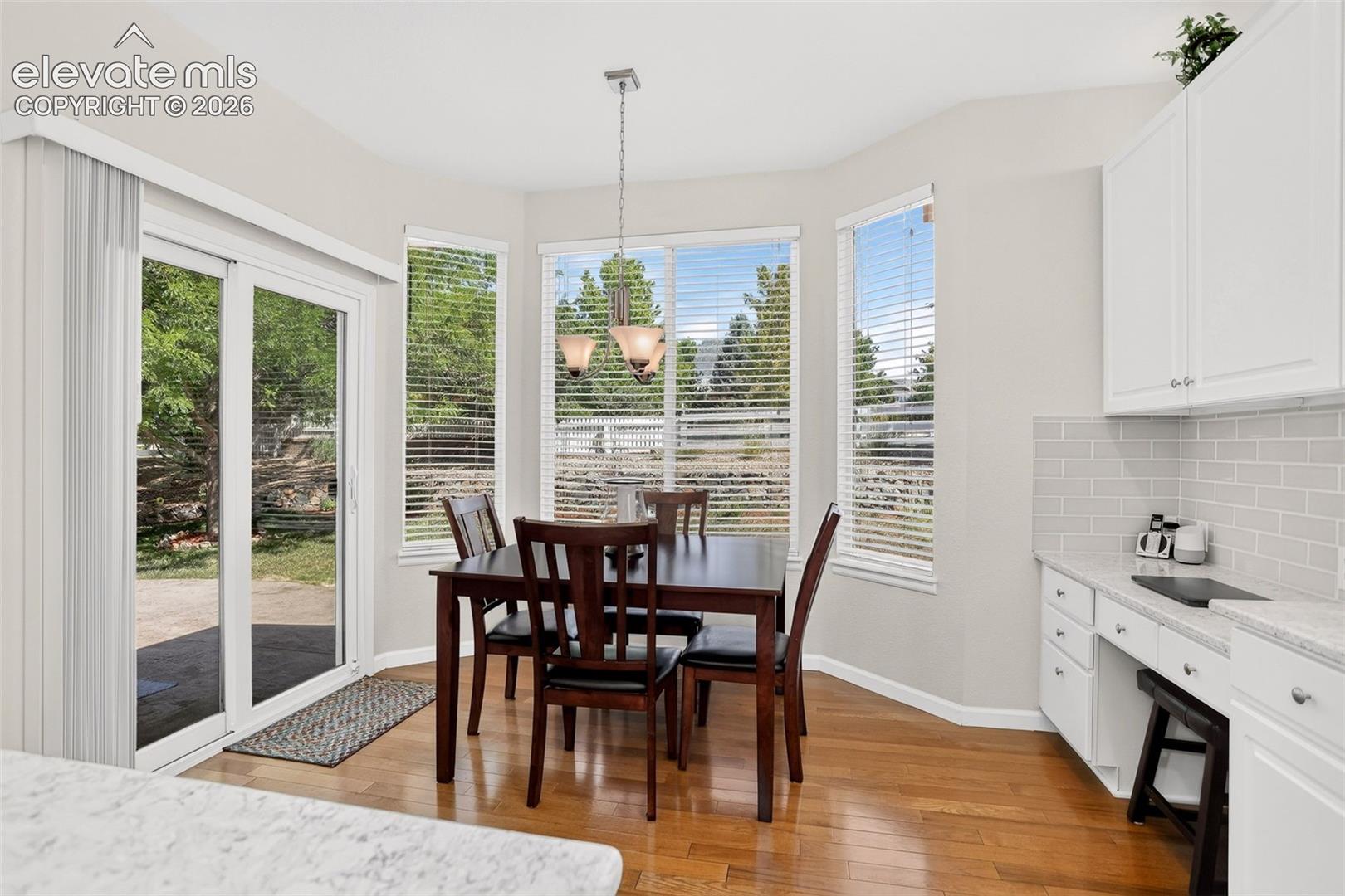 Light-filled dining area featuring wood-finish flooring, a contemporary chandelier, multiple windows, and sliding glass doors