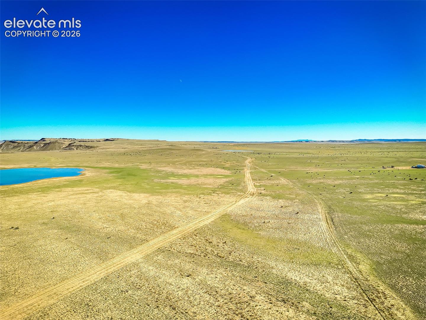 Expansive acreage featuring natural grasslands, rolling topography, a dedicated dirt access path, and frontage along a body of water