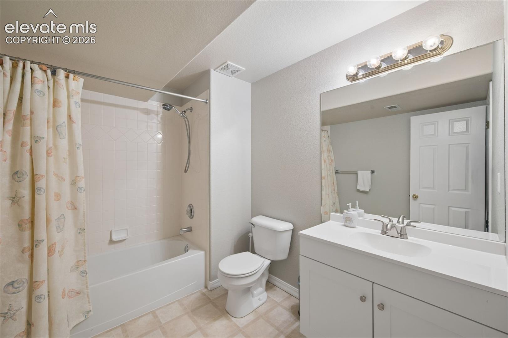 Bathroom featuring a white vanity with an integrated basin, a large wall-mounted mirror, a tub and shower combination with a surround, and multi-bulb lighting