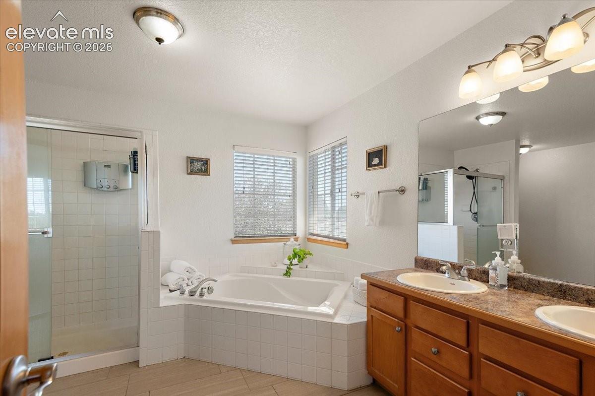 Bathroom featuring a soaking tub with tiled surround, a glass-enclosed shower, dual vanity with undermount sinks, wood cabinetry, and a large wall mirror