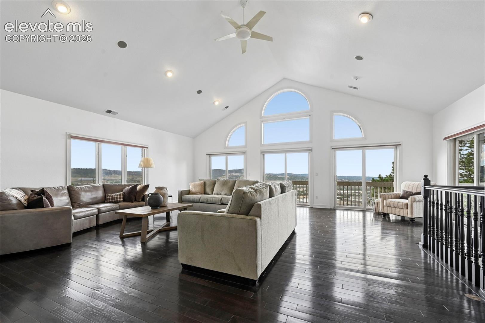 Spacious living area featuring high vaulted ceilings, recessed lighting, dark wood-finish flooring, and expansive windows