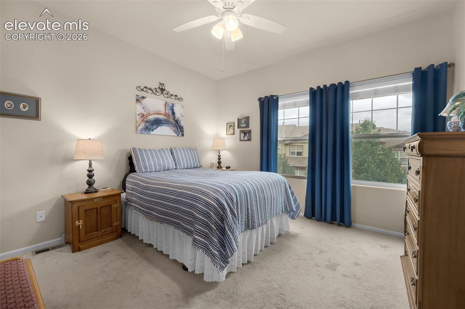 Carpeted bedroom with a vaulted ceiling and a pair of large windows, and neutral wall paint