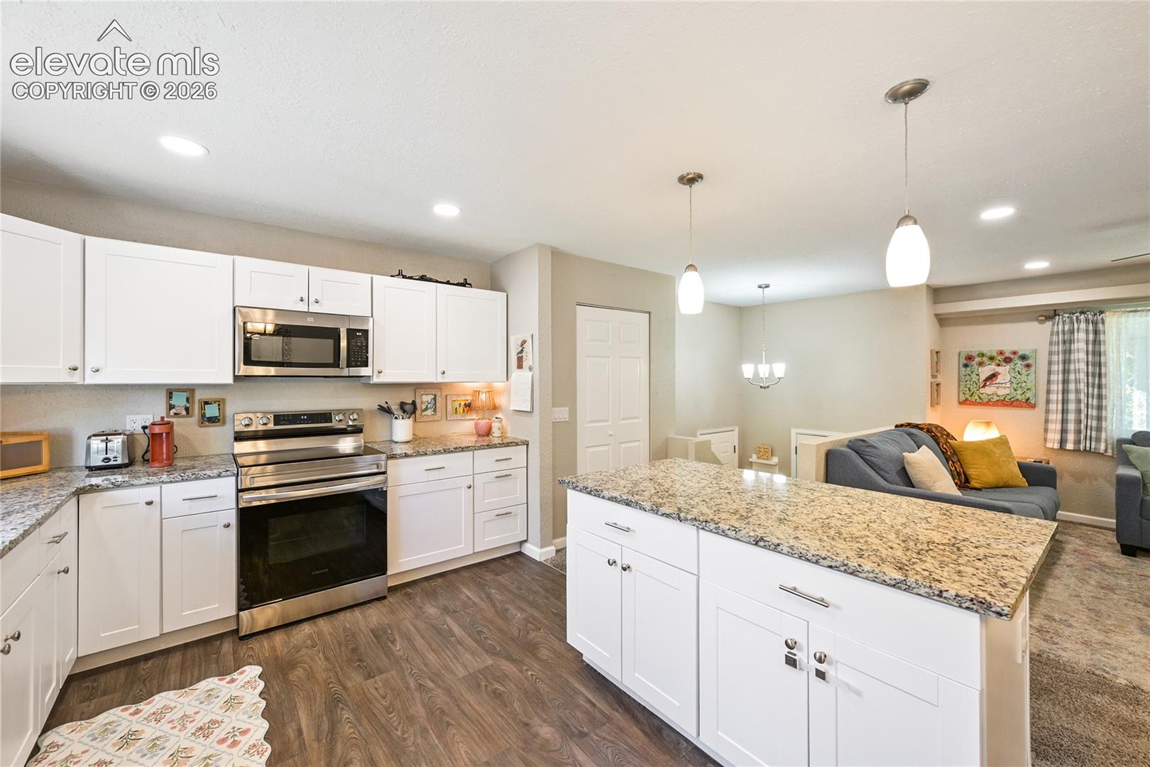 Kitchen featuring white cabinetry, speckled stone countertops, an oversized central island, stainless steel appliances, and wood-finish flooring
