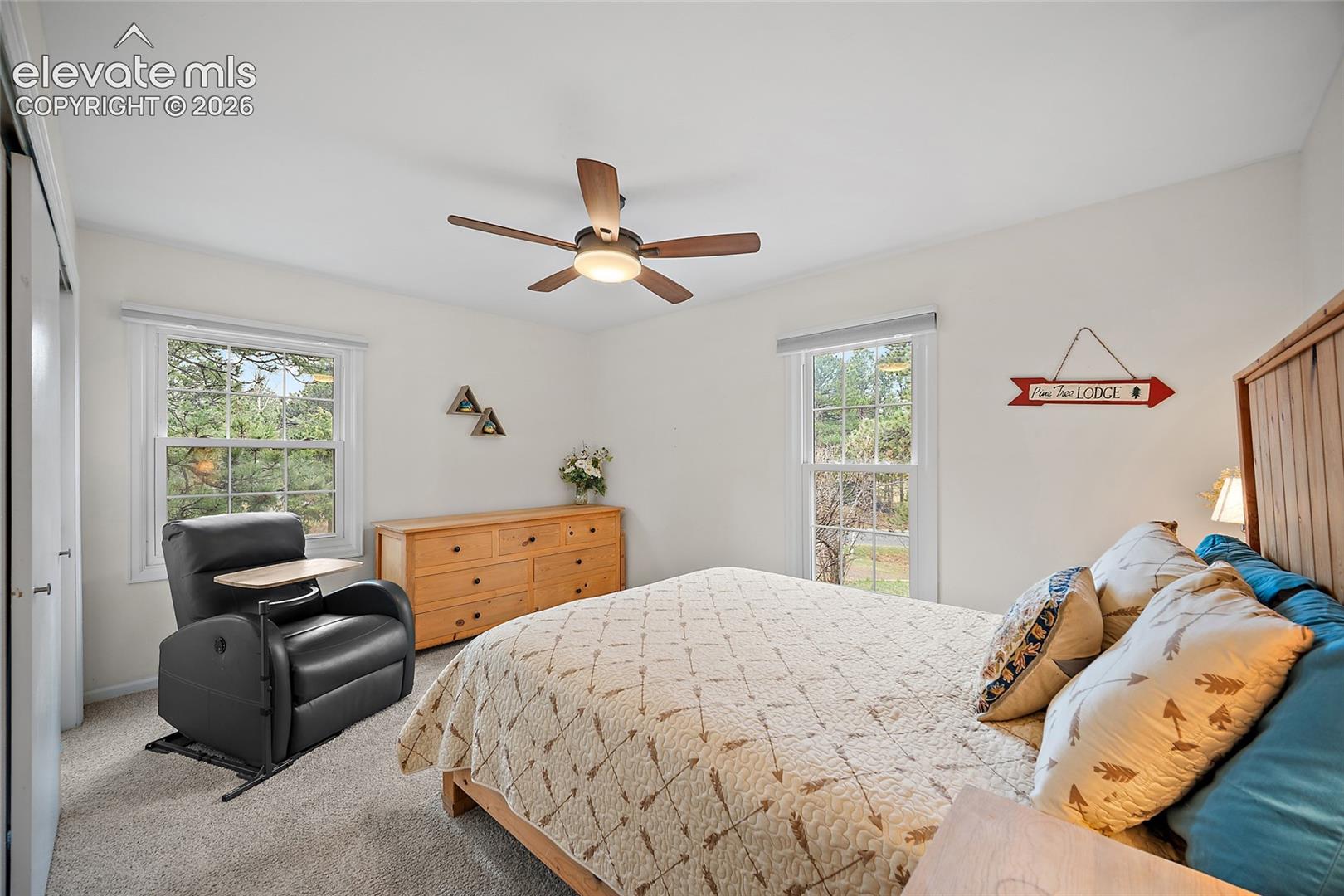 Neutral-toned interior space featuring light-colored wall-to-wall carpeting, dual double-pane windows, a central ceiling fan with integrated lighting, and white sliding-door closet storage