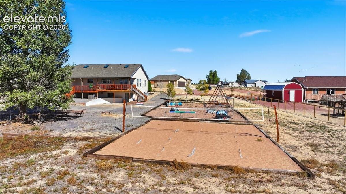 Volleyball-Expansive outdoor space featuring a sand volleyball court, a built-in climbing structure, a detached storage shed, and a wooden elevated deck