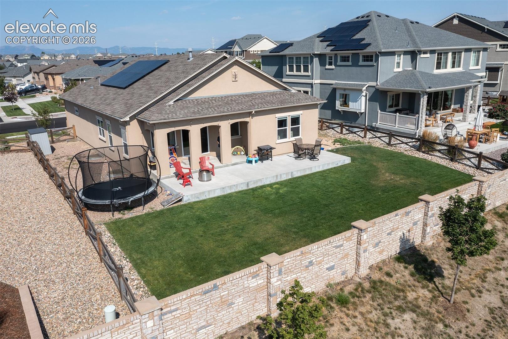 Stucco exterior with a concrete patio, a private yard with a stone-accented perimeter wall, and solar panels