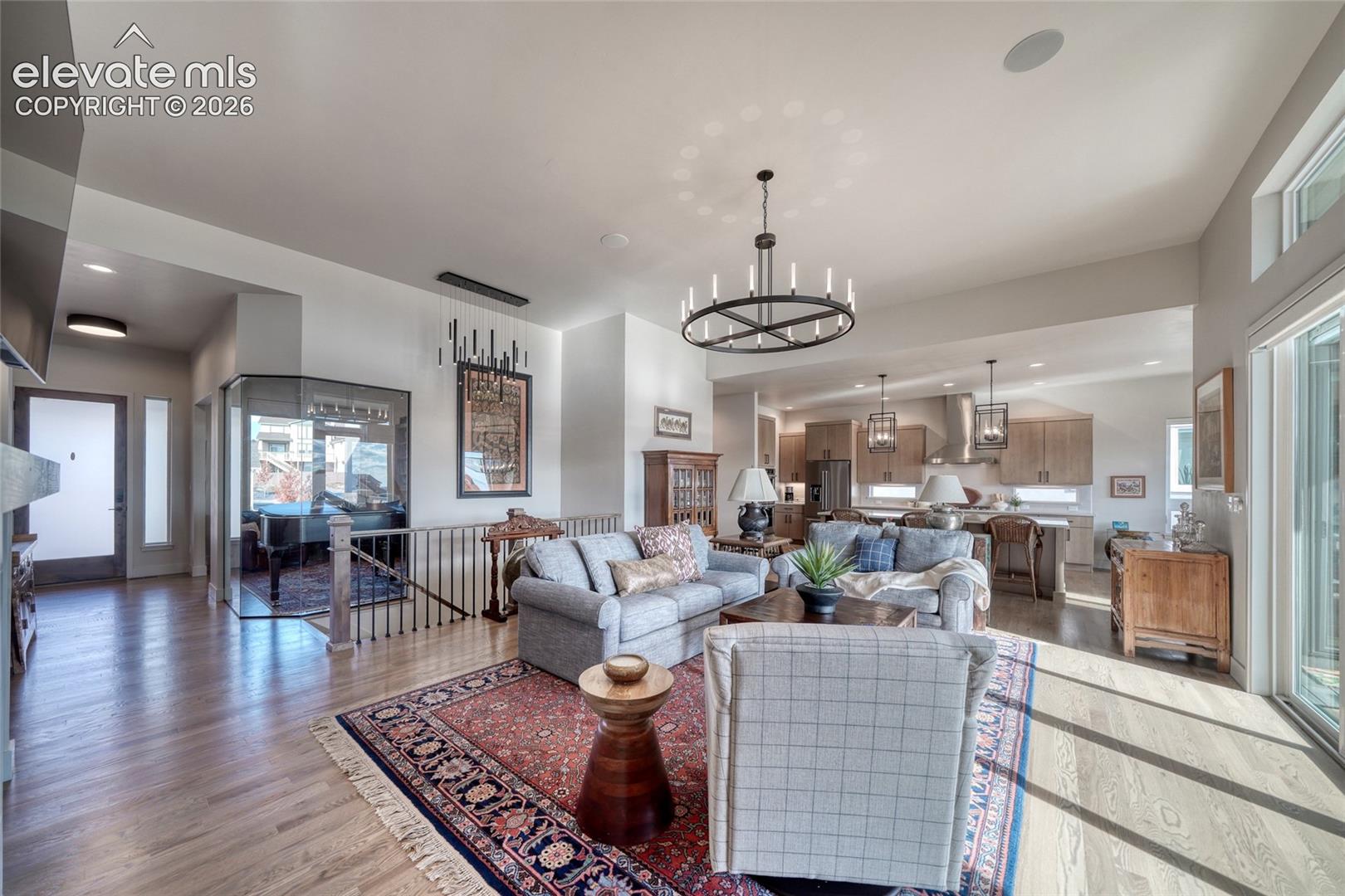 Open-concept interior featuring wood-finish flooring, a contemporary circular chandelier, glass-paneled wall accents, and high ceilings