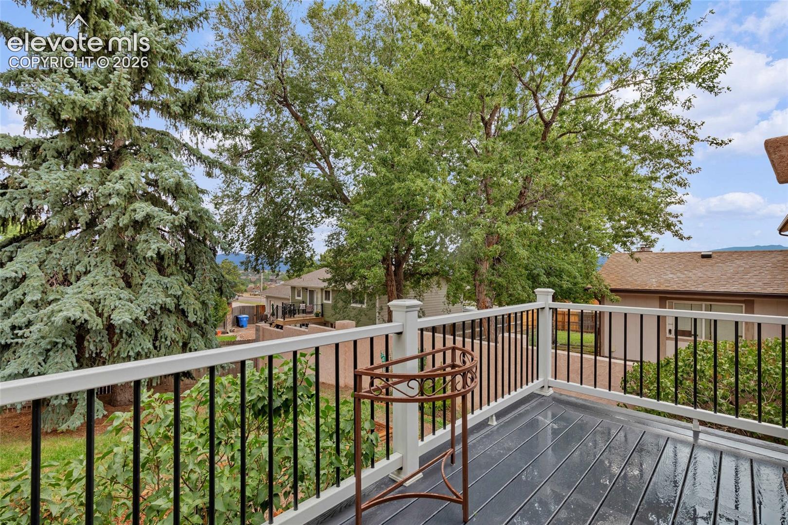 Outdoor deck featuring dark composite decking, white railing with black balusters, and mature surrounding trees