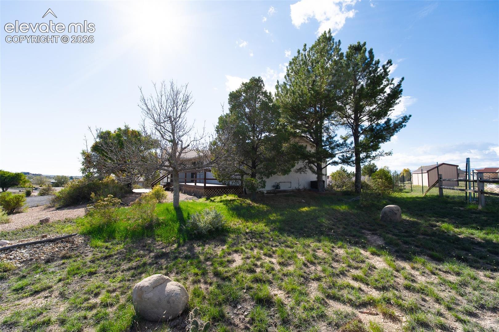 Expansive grounds featuring mature evergreen trees, indigenous landscaping, decorative boulders, and a wooden deck