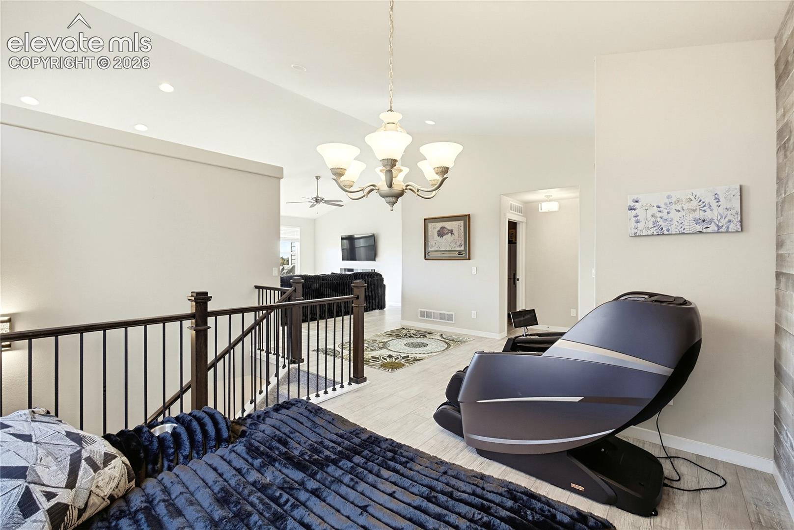 Open-concept interior featuring light wood-finish flooring, a wrought-iron staircase railing, a multi-arm chandelier, and a decorative wood-plank accent wall