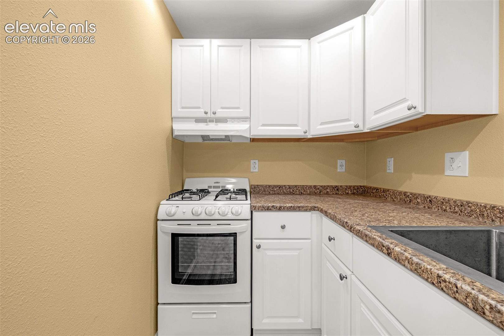 Kitchen featuring white shaker-style cabinetry, a gas range, integrated range hood, speckled-finish laminate countertops, and a stainless steel sink