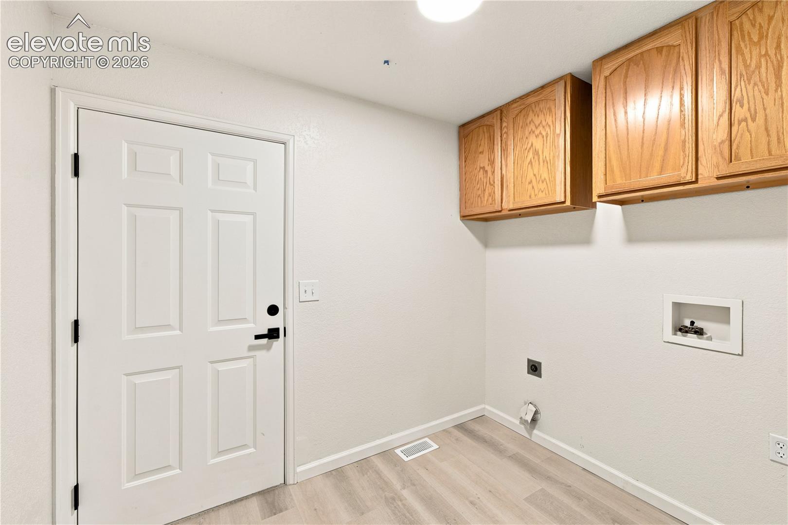 Utility room featuring wood-finish cabinetry, light wood-finish flooring, a white paneled door with black hardware, and appliance hookups