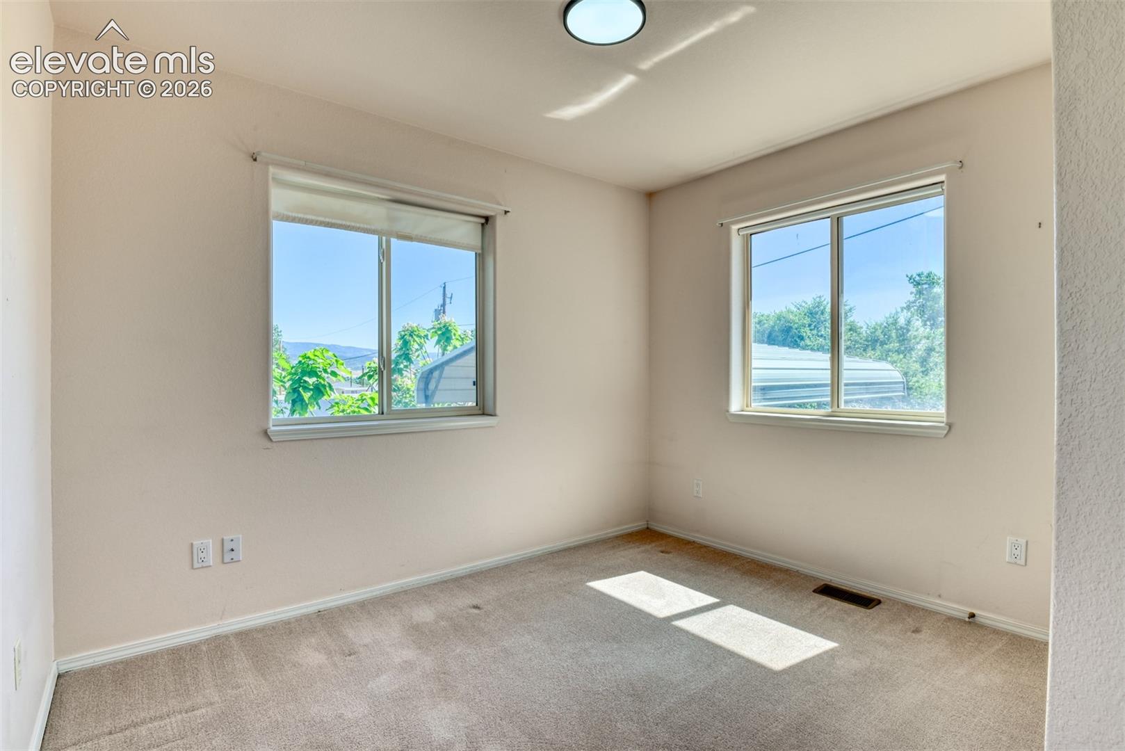 Neutral-toned interior space featuring wall-to-wall carpeting, two sliding windows, and a flush-mount ceiling light