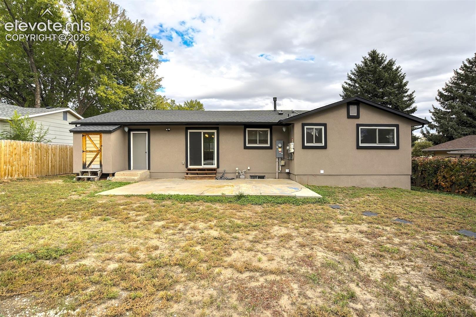 Exterior rear elevation featuring a concrete patio, sliding glass door, and a wood privacy fence
