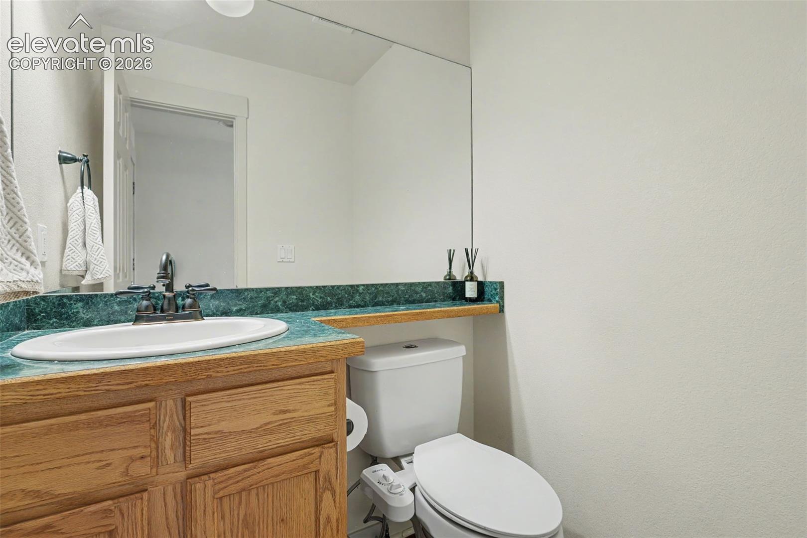 Bathroom featuring a vanity with a white oval sink, wood-finish cabinetry, and a green countertop