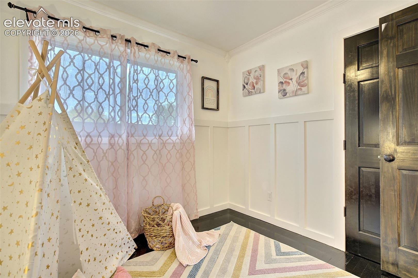 Room featuring wood-finish flooring, white board-and-batten wall detailing, crown molding, and a dark-stained six-panel door