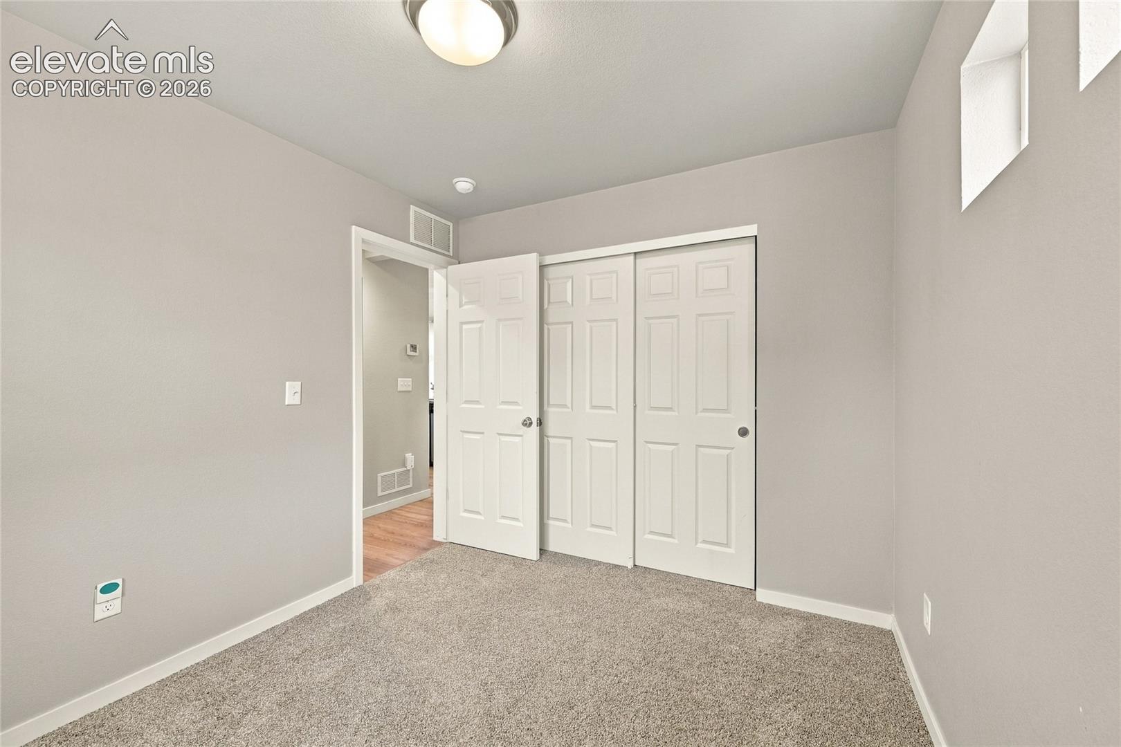 Carpeted room with light neutral wall paint, two-panel bifold closet doors, and an overhead flush-mount light fixture