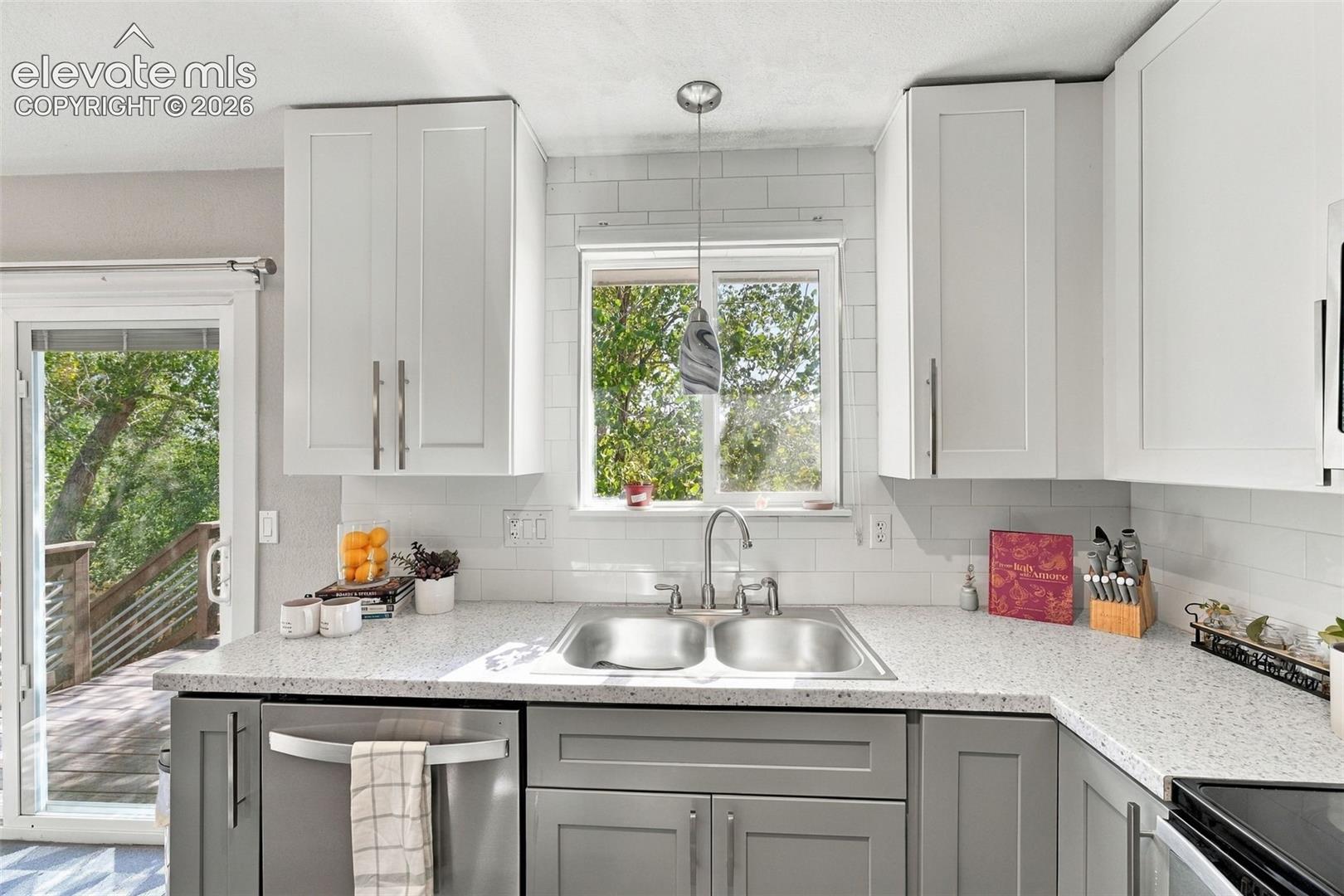 Kitchen featuring light and dark cabinetry, a dual basin stainless steel sink with a gooseneck faucet, light-toned countertops, and a subway tile backsplash