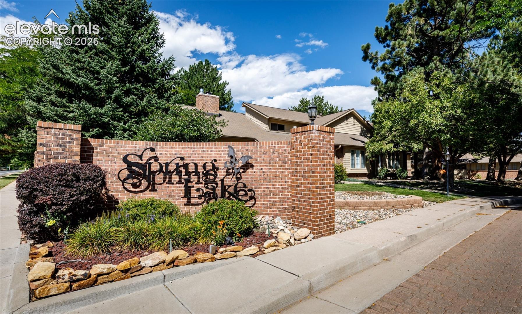 Brick entry monument with wrought iron lettering, complemented by mature landscaping and established trees