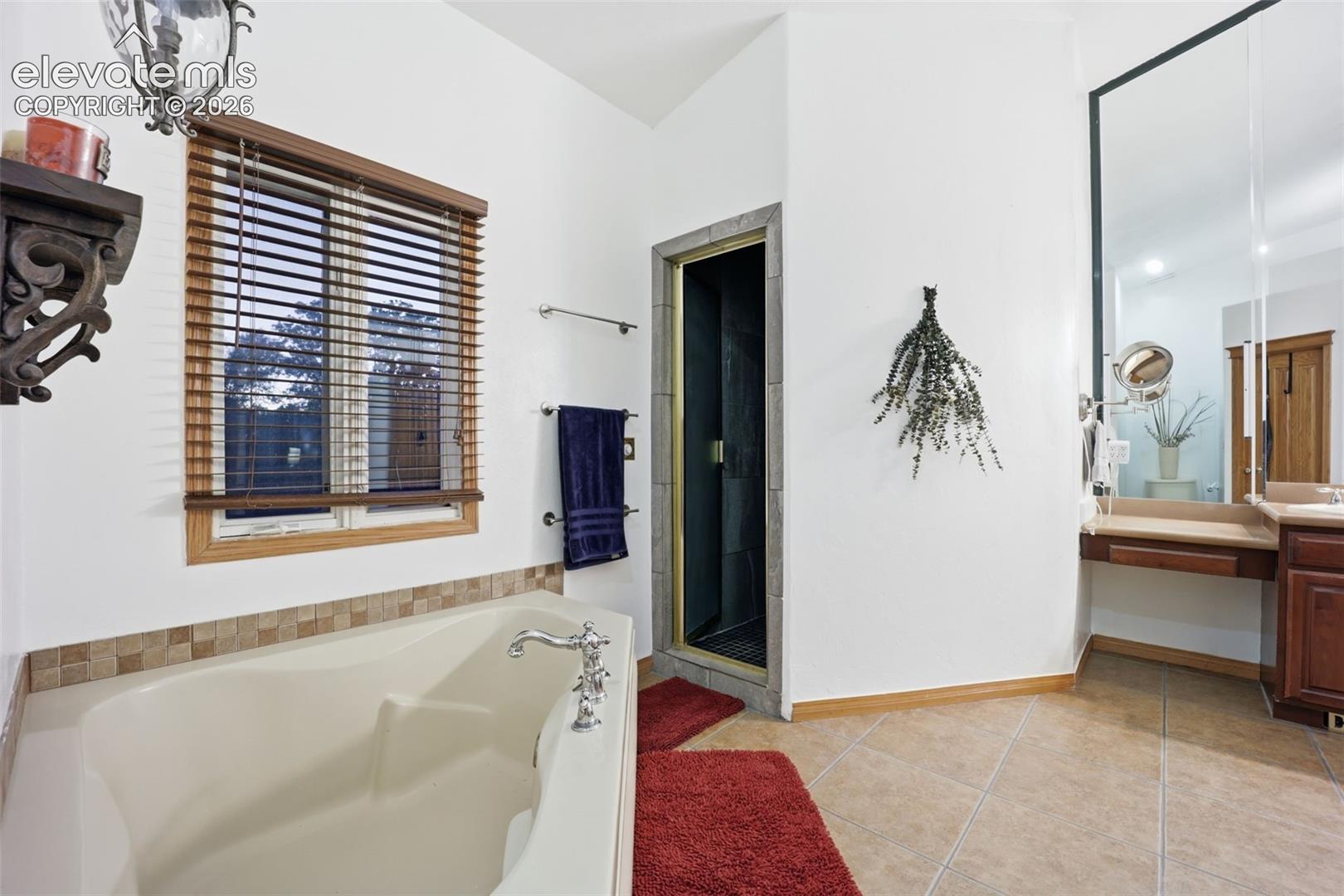 Built-in soaking tub with chrome fixtures, tiled surround, and wood-finish window blinds