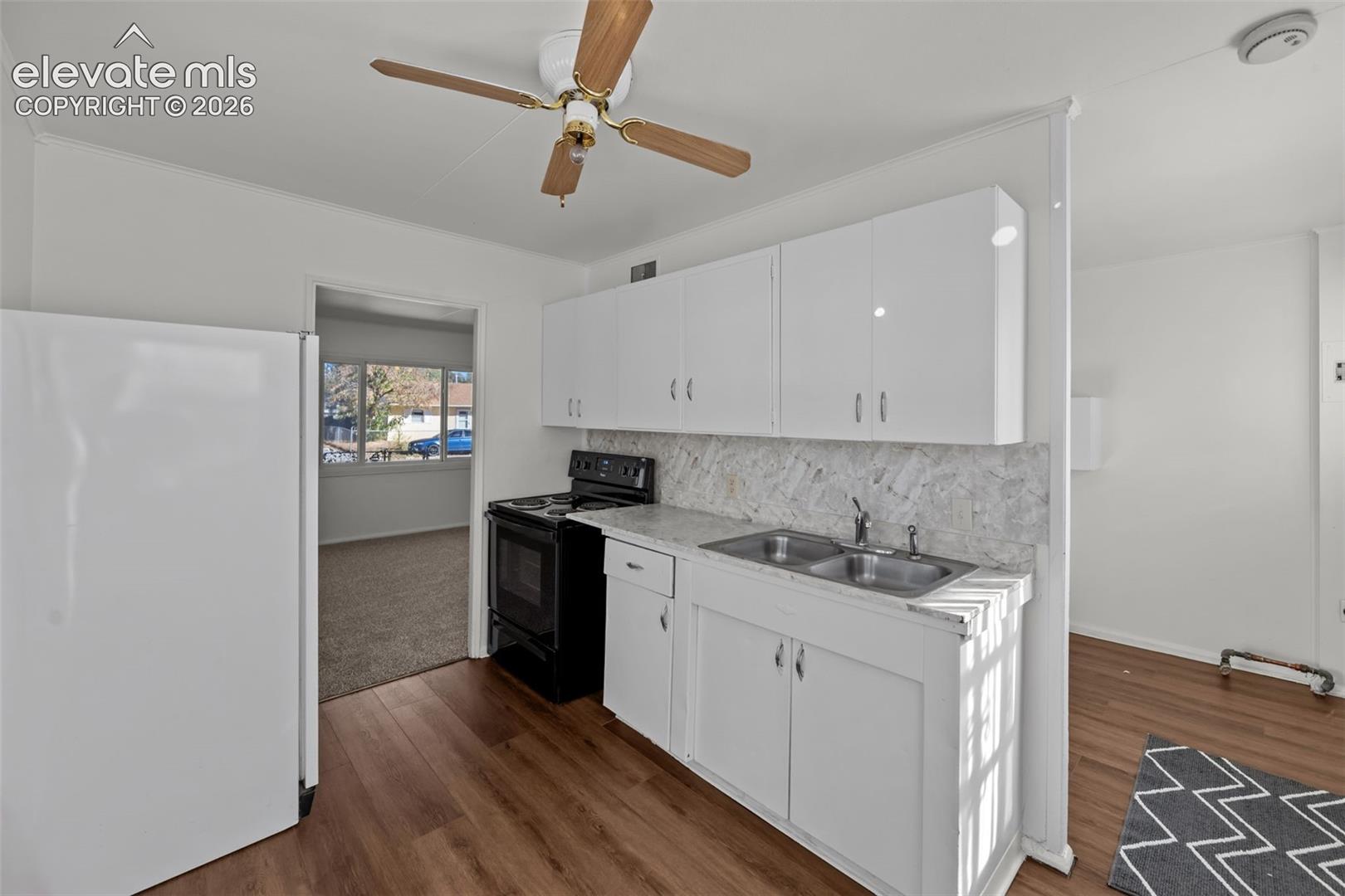 Kitchen featuring white cabinetry, wood-finish flooring, a stone-patterned backsplash, a double-basin stainless steel sink, and a ceiling fan