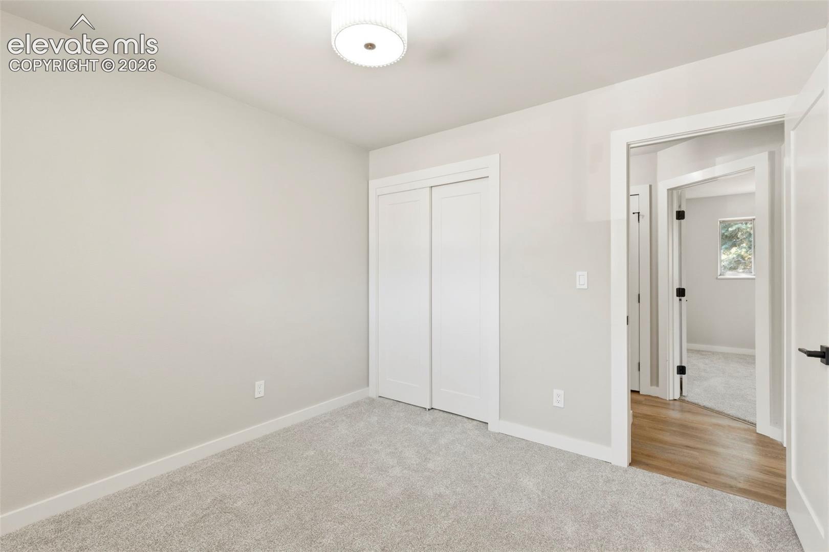 Neutral-toned room featuring light taupe carpet, white baseboards, and a white ceiling with a contemporary flush-mount light fixture