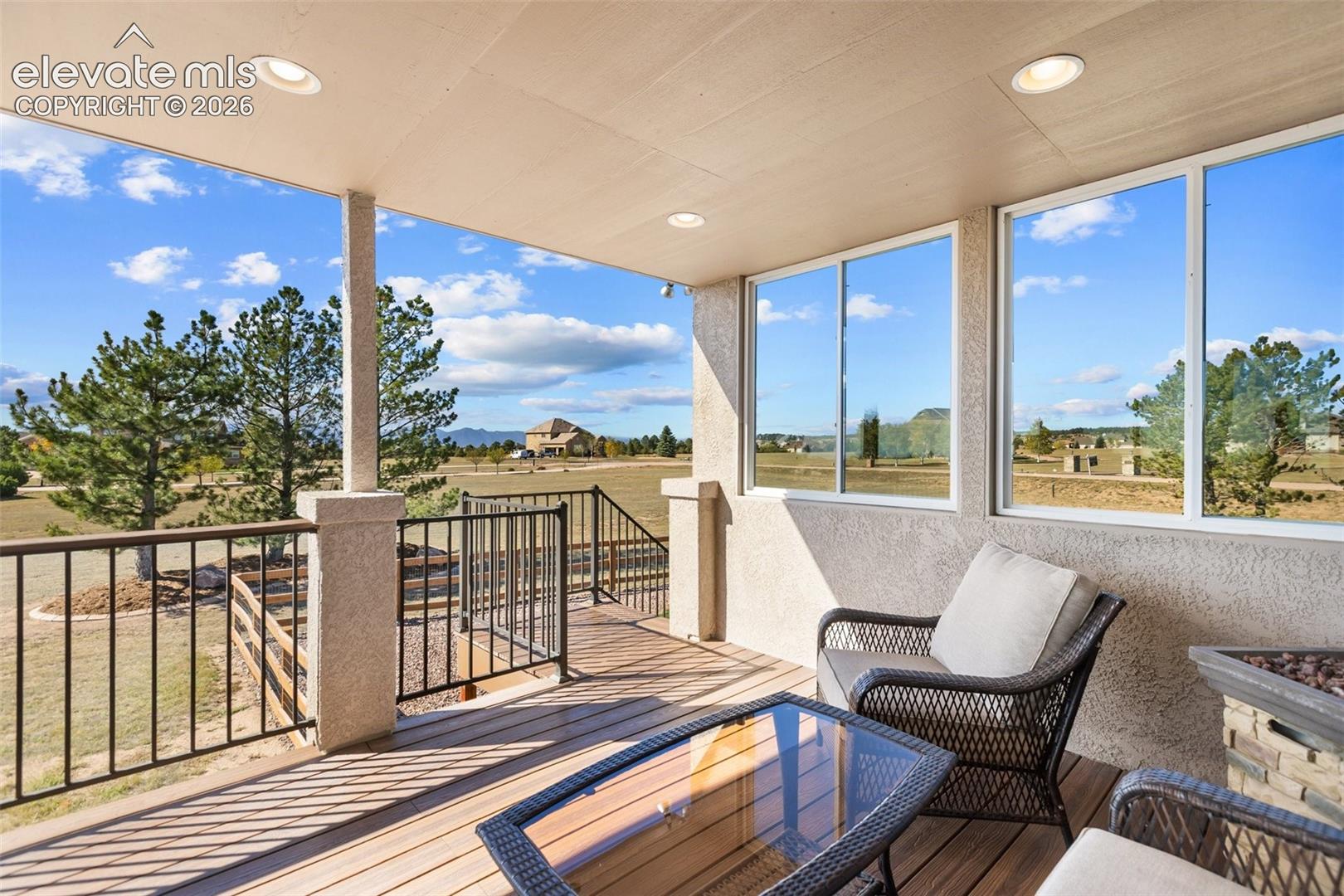 Covered outdoor patio featuring wood-finish decking, recessed ceiling lighting, a metal railing, and a stone-accented exterior wall