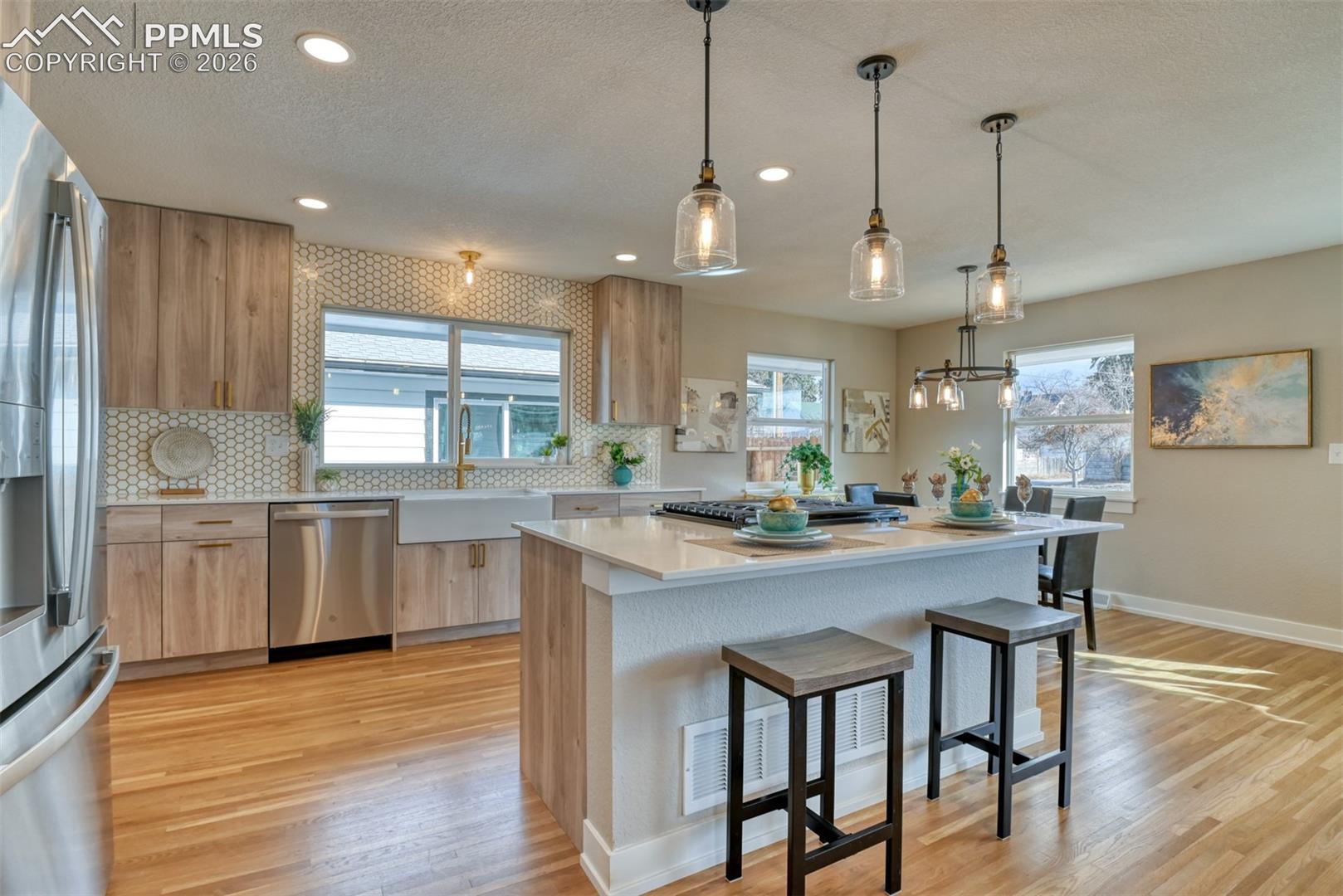 Kitchen with light stone countertops, modern cabinets, stainless steel appliances, a kitchen bar, and hanging light fixtures