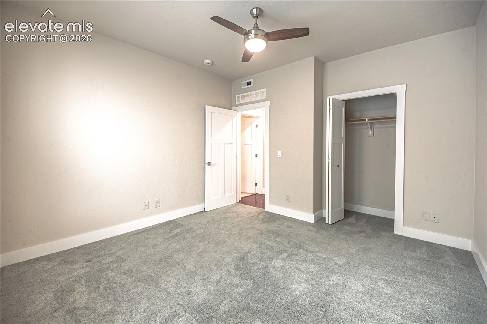Carpeted room featuring a ceiling fan with integrated lighting, a paneled door entry, a bi-fold closet door, and crisp white trim