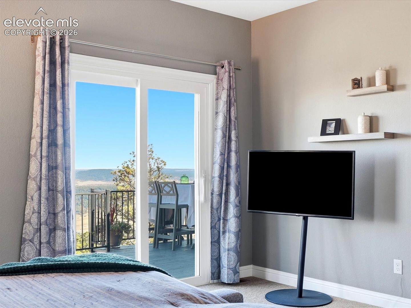 Sliding glass door with natural scenery, wall-mounted floating shelving, and neutral-toned wall paint