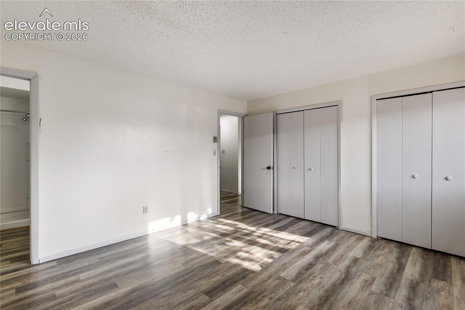Room featuring wood-finish flooring, two sets of bi-fold closet doors, a flat white ceiling, and a doorway