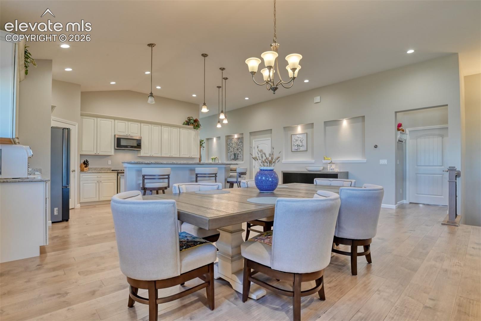 Open-concept living area featuring wood-finish flooring, recessed lighting, a chandelier, and a kitchen with white cabinetry and granite countertops.