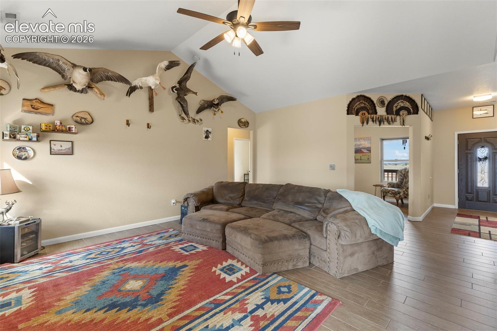 Vaulted ceilings featuring a central light fixture with a ceiling fan, wood-finish flooring, and an entry door with decorative glass inlay