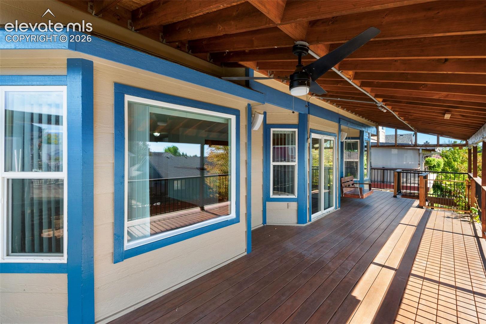 Expansive covered deck featuring wood-finish flooring, exposed wood beam ceiling, multiple windows, and a ceiling fan
