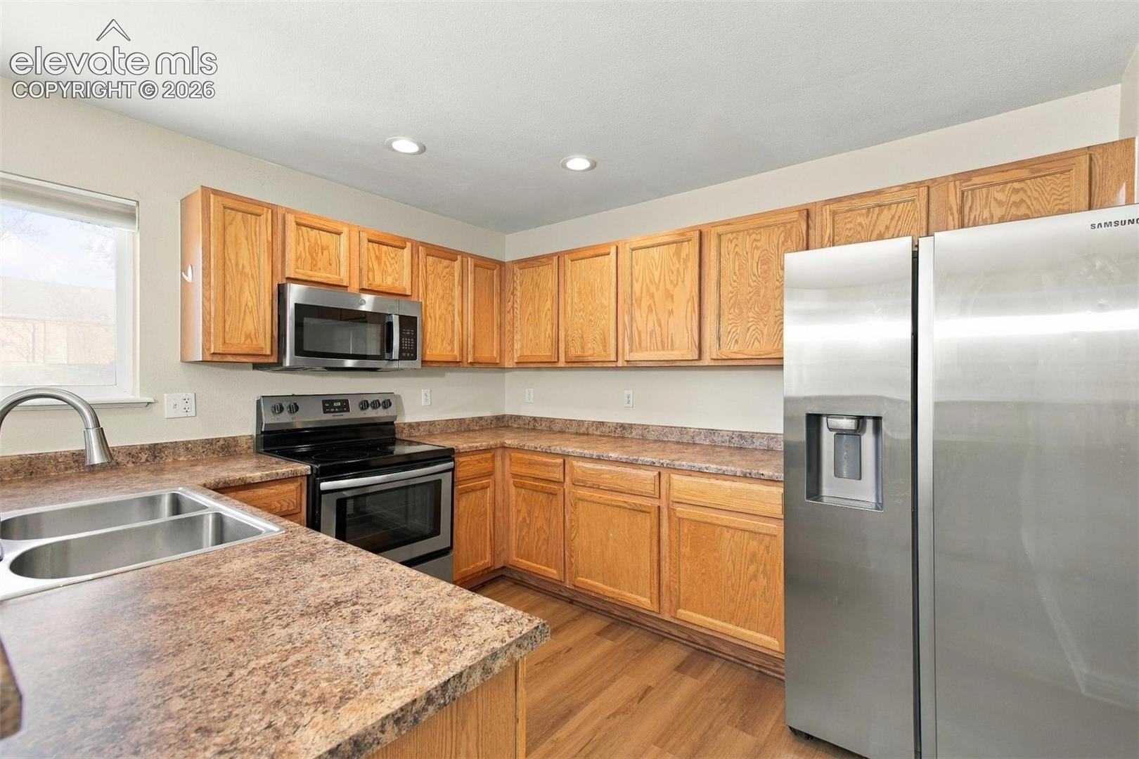Kitchen featuring wood cabinetry, laminate countertops, stainless steel appliances, a double-basin sink with a gooseneck faucet, and wood-finish flooring