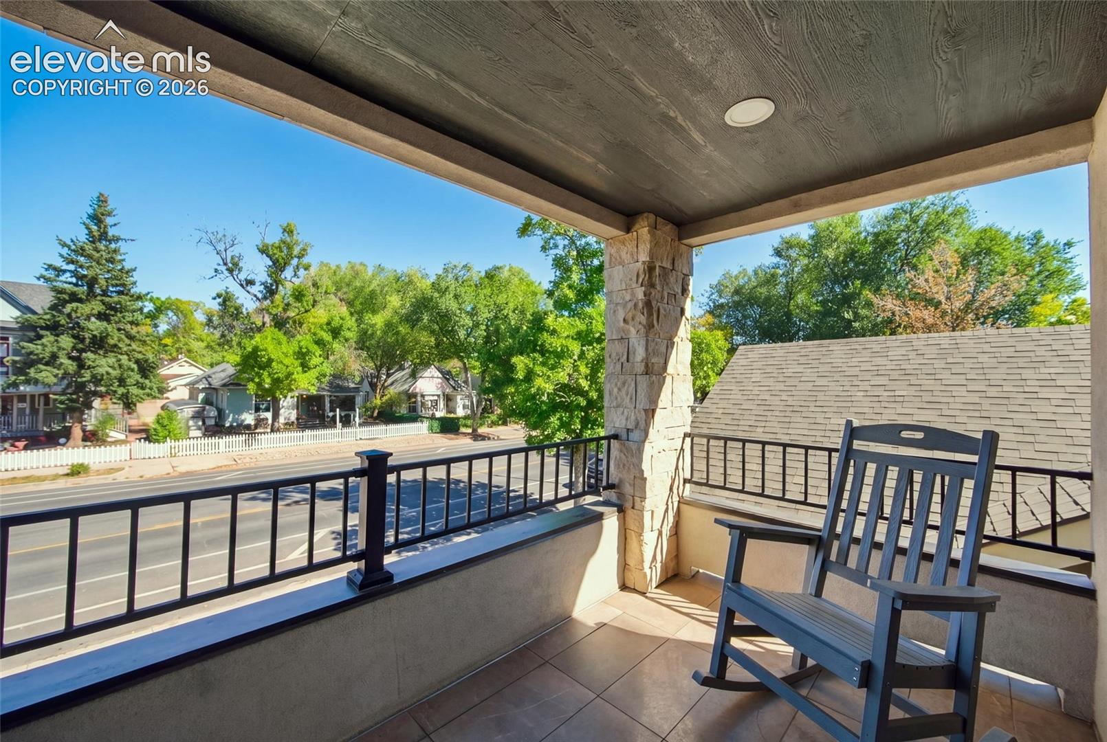 Covered balcony featuring tile flooring, stone-veneer pillar, recessed lighting, and black metal railings
