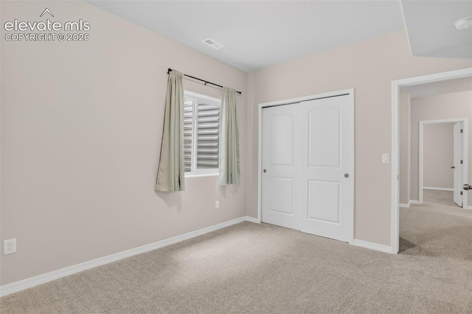Carpeted room with a window featuring horizontal blinds, light-toned walls, white trim, and a white bi-fold closet door