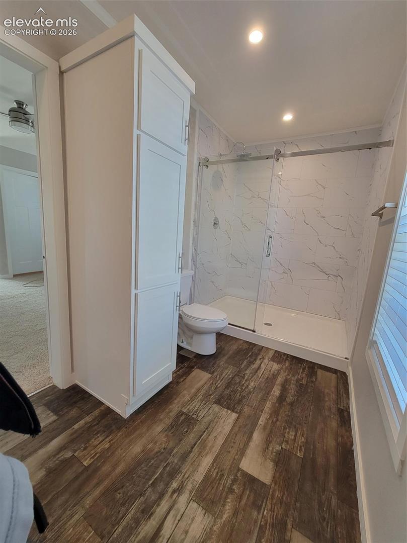 Walk-in shower with sliding glass doors, floor-to-ceiling stone-patterned wall surround, tall built-in storage cabinetry, and wood-finish flooring