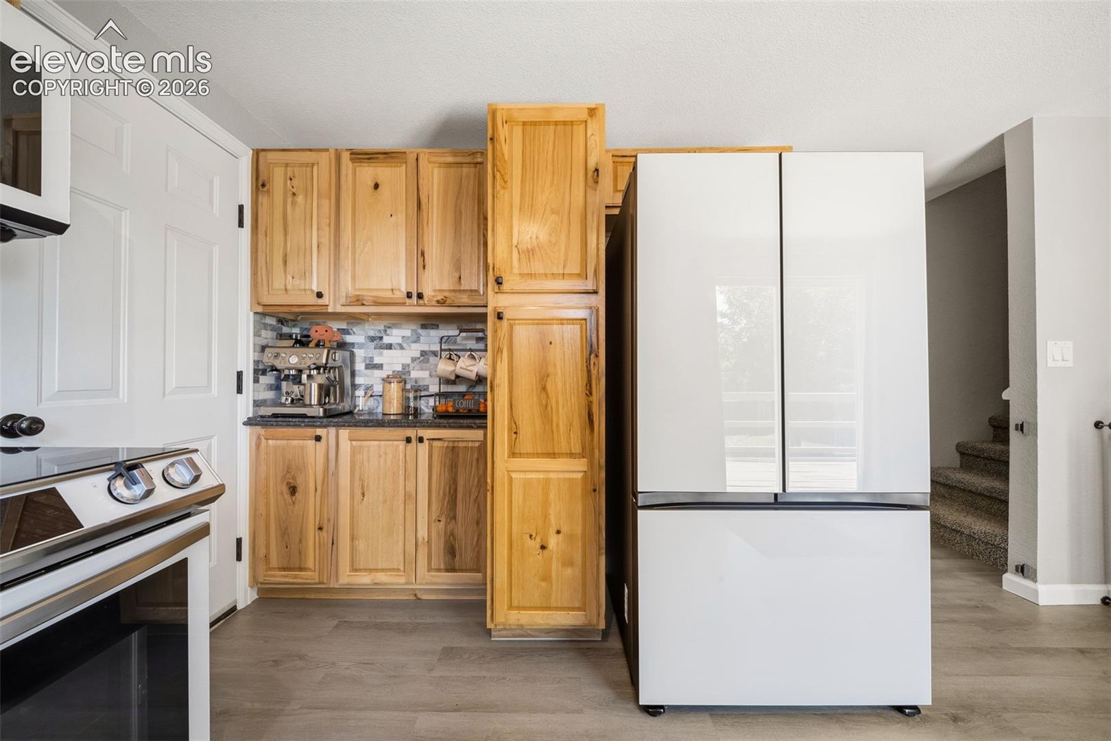 Wood-finish flooring, wood cabinetry with black hardware, tile backsplash, built-in wall cabinetry, and a modern refrigerator