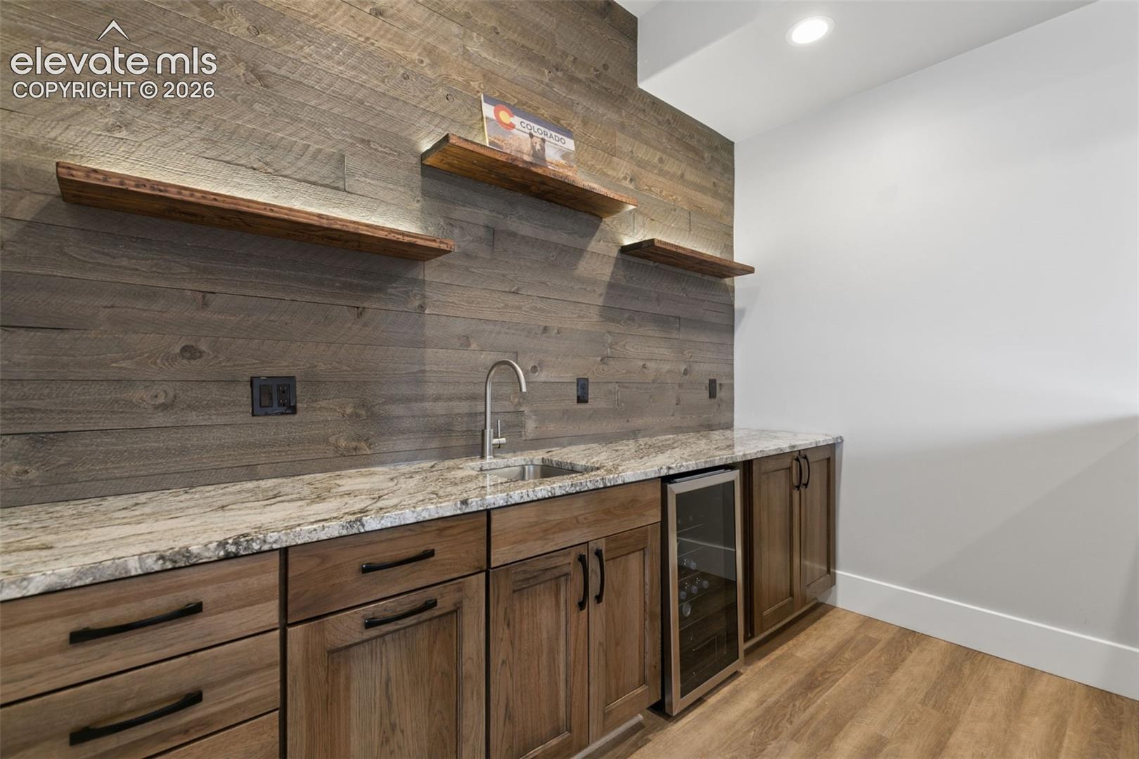 Wood-finish flooring, built-in cabinetry, stone countertop, integrated beverage refrigerator, and a stainless steel sink with a gooseneck faucet
